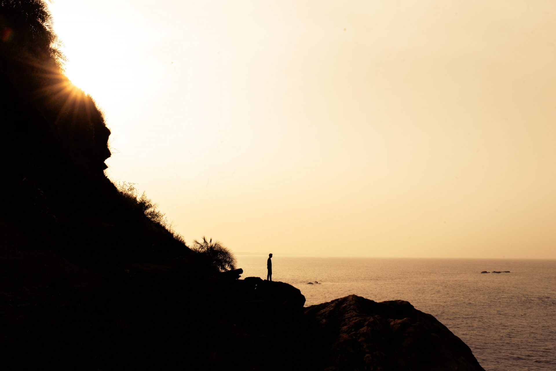 man standing on the edge of a cliff near beach and ocean